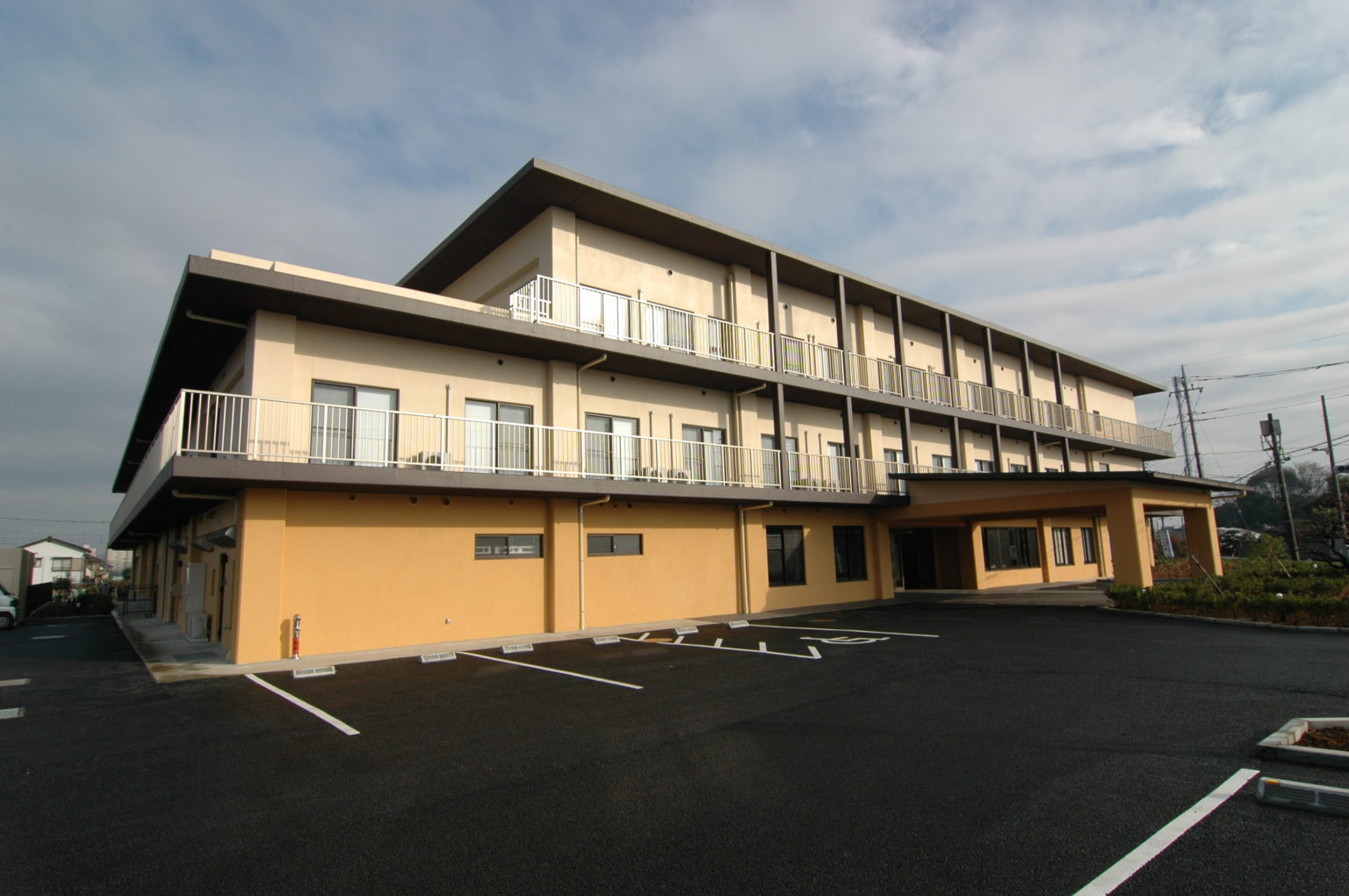 3階建ての介護施設の建物外観。黄色と白のツートンカラー、駐車場完備。