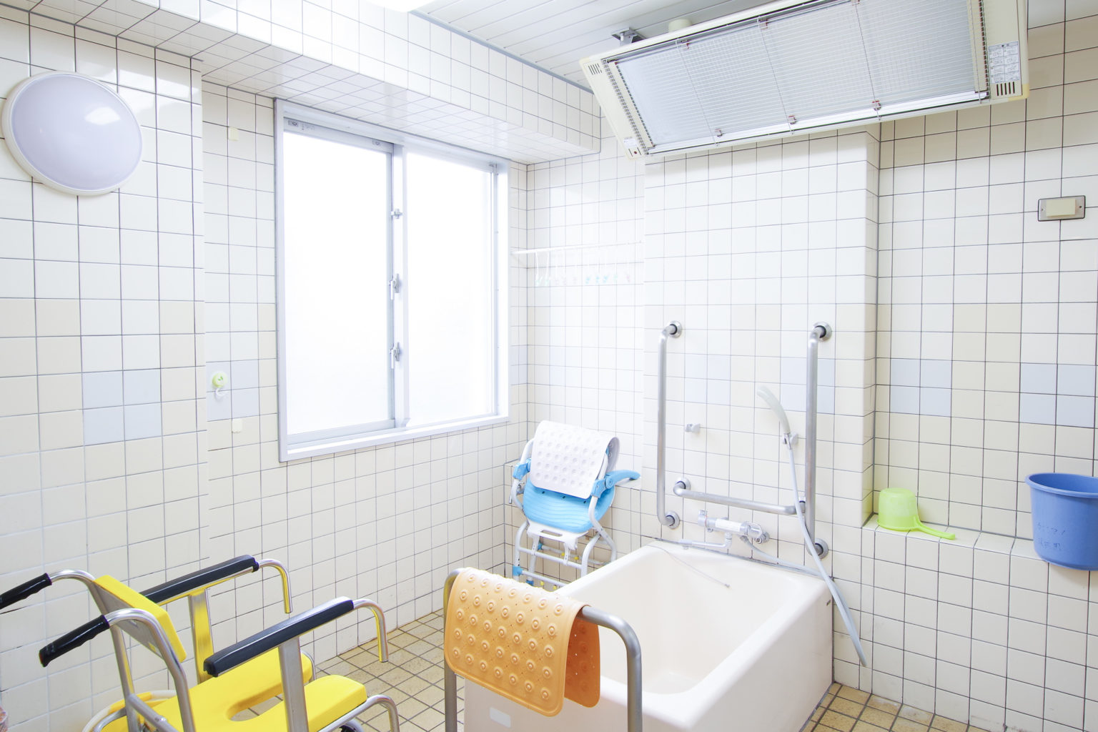 介護施設の浴室。白いタイル張りで清潔感があり、入浴補助用の機器や手すりが備わっている。