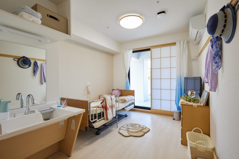 介護施設の個室。洗面台、ベッド、収納が備わった広々とした居住空間。